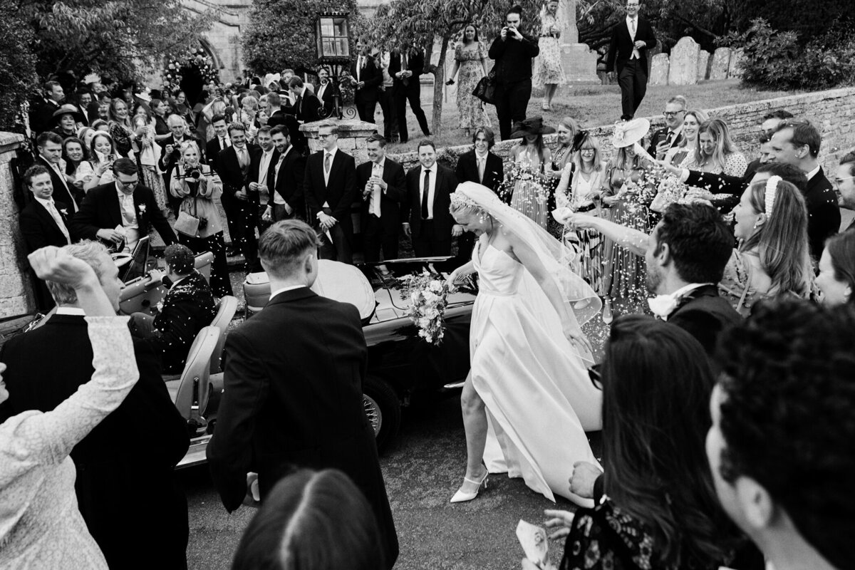 bride smiling getting into a car with confetti being thrown